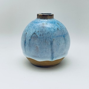 Könnte beinhalten: Eine kleine, runde Keramikvase mit hellblauer Glasur und braunem Rand. Die Vase hat eine leicht unebene, strukturierte Oberfläche.