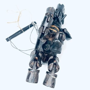 May include: A wooden puppet with articulated limbs and a string attached to its head. The puppet is painted black and has a weathered appearance.