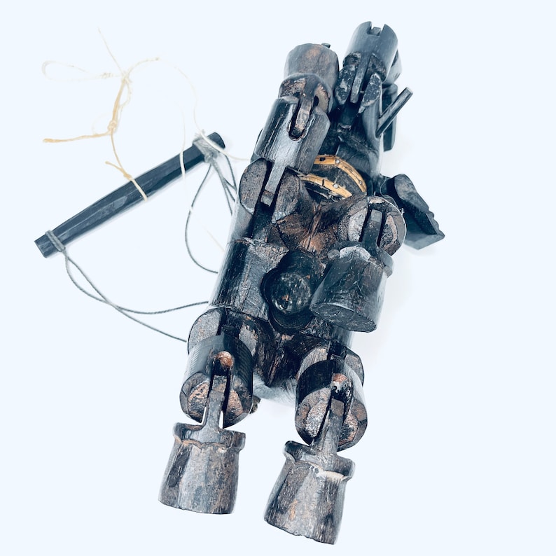 May include: A wooden puppet with articulated limbs and a string attached to its head. The puppet is painted black and has a weathered appearance.