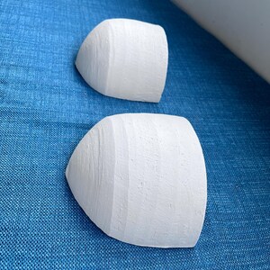 May include: Two white, semi-circular objects with a textured surface, possibly architectural elements or decorative pieces, are arranged on a blue textured fabric. The objects have a rounded shape and a flat back.