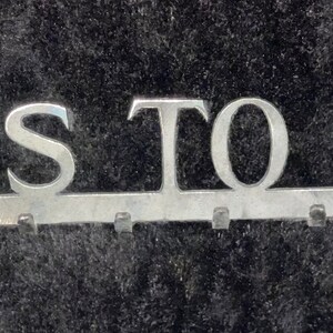 May include: A silver metal key rack with the words "KEYS TO LIFE" in large letters. The rack has multiple hooks for hanging keys.