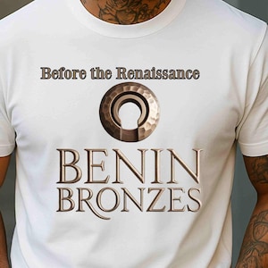 May include: White t-shirt with the text "Before the Renaissance" above a circular design and the words "BENIN BRONZES" in a bronze color. The shirt is short-sleeved.