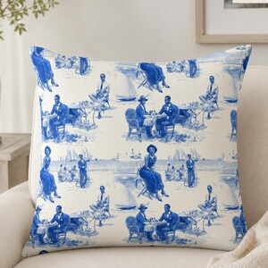 May include: A square throw pillow measuring 20 inches by 20 inches, featuring a repeating blue and white toile-style pattern. The design depicts various scenes of people sitting at tables and standing near sailboats on a beach setting.