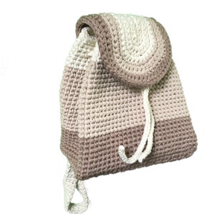 Op de afbeelding: Een gehaakte rugzak in beige en wit. De rugzak heeft een trekkoord sluiting en een klep met een afgeronde bovenkant.