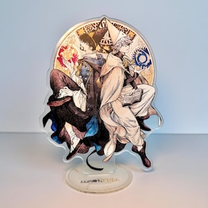 May include: An acrylic standee featuring two illustrated characters back-to-back in a circular frame. One character wears dark robes with fire, the other wears light robes with a pointed hat and holds a book. The base displays the text "とんがり帽子のアトリエ".
