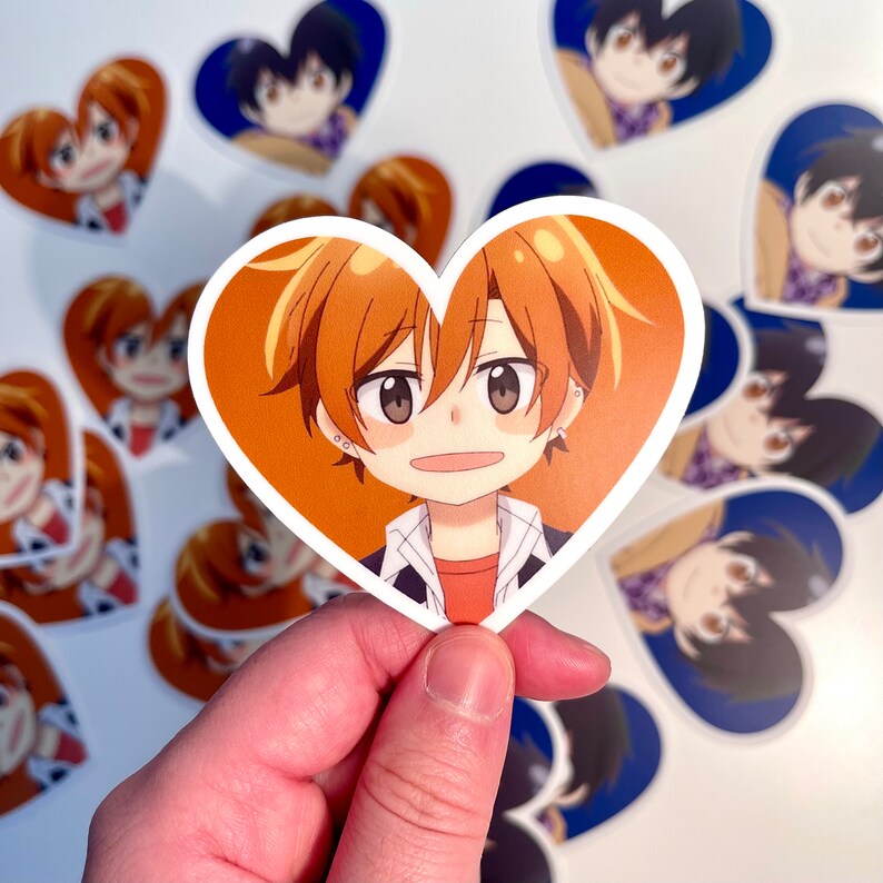 May include: A heart-shaped sticker featuring a cartoon character with orange hair, brown eyes, and a light pink shirt. The character is smiling and has a light blue collar and a dark blue jacket. The sticker is surrounded by other heart-shaped stickers with different cartoon characters.