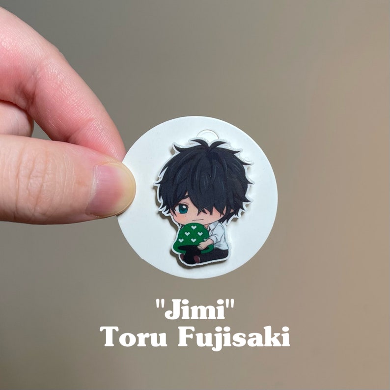 May include: A white circle sticker with a cartoon illustration of a boy with black hair holding a green mushroom with white hearts. The text "Jimi" and "Toru Fujisaki" is printed below the image.