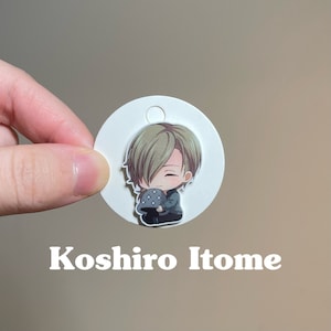 May include: A white circle with a hole at the top, featuring a cartoon illustration of a character with green hair, holding a mushroom. The text "Koshiro Itome" is printed below the circle.