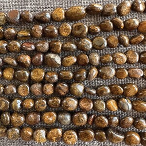 Könnte beinhalten: Eine Strähne aus braunen und goldenen Tigerauge-Edelsteinkugeln. Die Kugeln sind glatt und poliert und haben eine natürliche, organische Form.