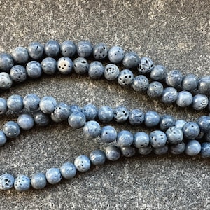 Könnte beinhalten: Eine Schnur aus blauen Lavasteinen mit poröser Textur. Die Perlen sind rund und haben eine matte Oberfläche.