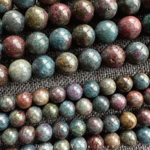 Könnte beinhalten: Eine Reihe runder, mehrfarbiger Edelsteinperlen. Die Perlen sind eine Mischung aus Grün, Blau und Pink mit einer gesprenkelten, marmorierten Optik.