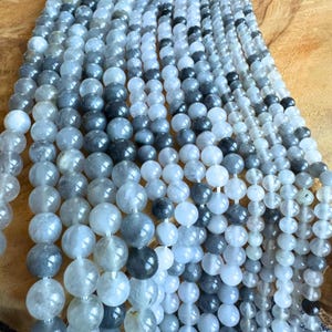 Könnte beinhalten: Mehrere Stränge runder Edelsteinperlen in Grau-, Weiß- und Schwarztönen. Die Perlen sind aufgefädelt und erzeugen einen geschichteten Effekt. Diese Perlen dienen wahrscheinlich zur Schmuckherstellung.