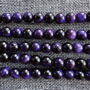 May include: Close-up of strands of polished gemstone beads. The beads alternate between deep purple and black, creating a striking contrast. The round beads are arranged in neat rows, showcasing their glossy surfaces and natural variations.