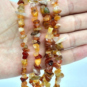 May include: Strands of gemstone beads in shades of orange, yellow, and brown. The beads are irregular in shape and size, strung together to create a necklace or bracelet. The gemstones have a polished, natural appearance.