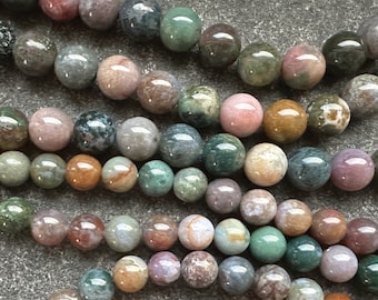 Pode incluir: Um fio de contas de ágata coloridas, com uma variedade de tons de verde, marrom, rosa e branco. As contas são redondas e lisas, com um acabamento natural e polido.