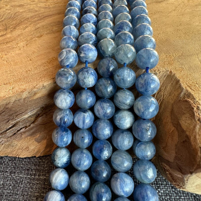 May include: A strand of blue kyanite beads. The beads are round and have a smooth, polished finish. They are strung on a clear elastic cord.