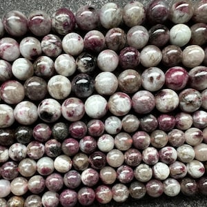 May include: A collection of round gemstone beads in pink, white, and brown hues. The beads are polished and glossy, with varied colours and patterns. These beads are suitable for jewellery making.