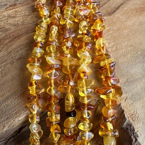May include: Close-up of several strands of amber-coloured beads. The beads are irregular in shape and vary in shades of yellow, orange, and brown. The beads are strung together, creating a necklace or bracelet.