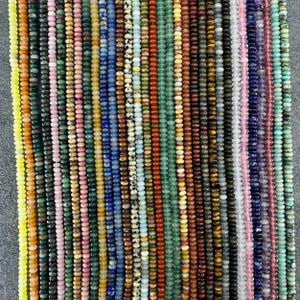 Könnte beinhalten: Eine Sammlung zahlreicher vertikaler Stränge aus kleinen, runden Edelsteinperlen in einer Vielzahl von Farben, darunter Gelb, Orange, Rosa, Blau, Grün, Braun, Schwarz, Weiß und Violett, die nebeneinander in einem dichten Muster angeordnet sind.