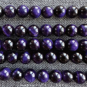 May include: Rows of polished, round beads in shades of deep purple and black. The beads have a glossy finish, reflecting light. The arrangement suggests a jewelry component, possibly for necklaces or bracelets.