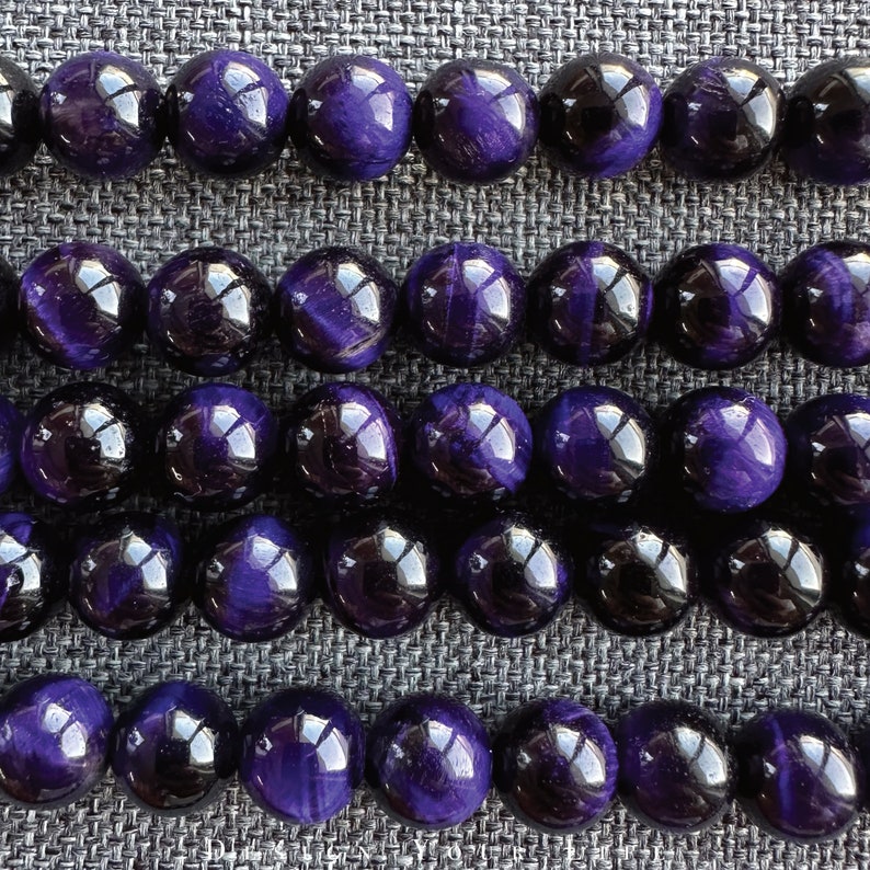 May include: Rows of polished, round beads in shades of deep purple and black. The beads have a glossy finish, reflecting light. The arrangement suggests a jewelry component, possibly for necklaces or bracelets.