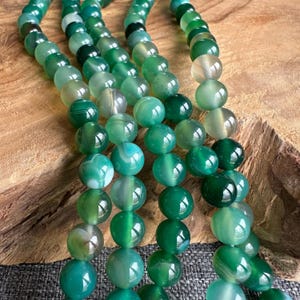 May include: A strand of green agate beads with white and green banding. The beads are round and smooth, and they are strung on a clear thread.