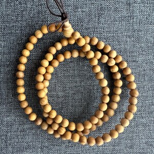 Puede incluir: Un collar de cuentas de madera marr&oacute;n claro con un cord&oacute;n marr&oacute;n. Las cuentas son redondas y est&aacute;n espaciadas uniformemente. El collar se muestra sobre una superficie gris texturizada.