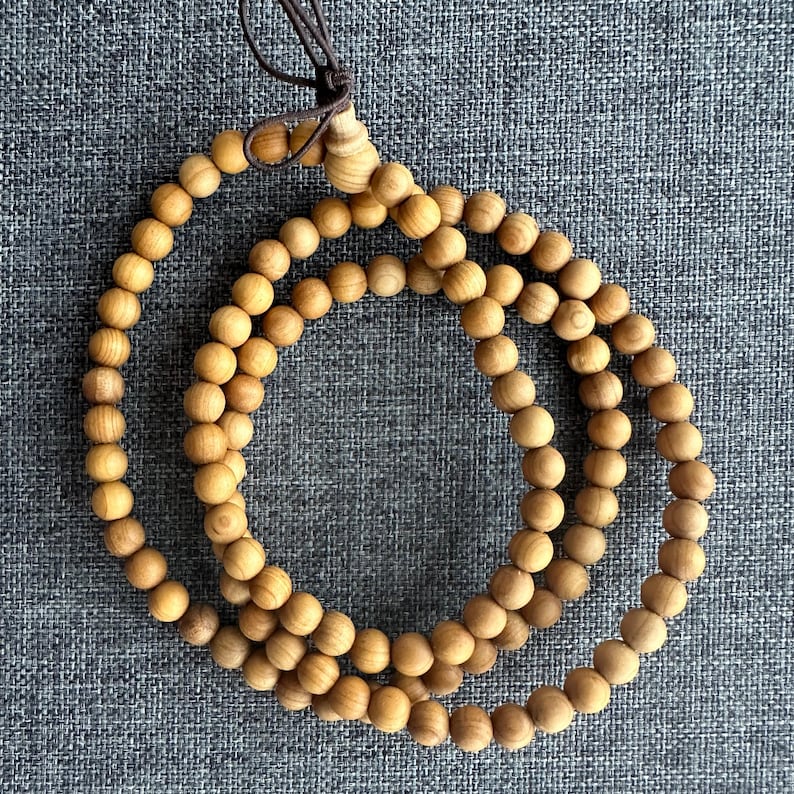 Puede incluir: Un collar de cuentas de madera marr&oacute;n claro con un cord&oacute;n marr&oacute;n. Las cuentas son redondas y est&aacute;n espaciadas uniformemente. El collar se muestra sobre una superficie gris texturizada.