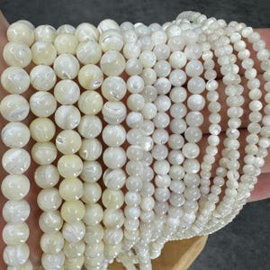 Op de afbeelding: Meerdere strengen crèmekleurige parelmoerkralen in verschillende maten. De kralen hebben een parelmoerglans en zijn aan elkaar geregen. Deze kralen zijn ideaal voor het maken van sieraden. De kralen worden in millimeters gemeten.