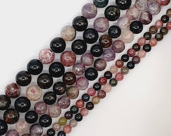 Pode incluir: Um fio de contas de pedras preciosas multicoloridas. As contas são redondas e têm uma variedade de cores, incluindo preto, rosa, roxo e verde. As contas são enfiadas em um fio transparente.