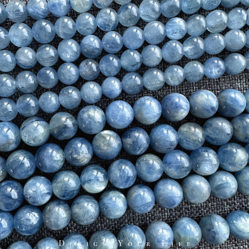 May include: A strand of light blue gemstone beads. The beads are round and have a smooth, polished finish. They are arranged in a loose, flowing pattern.