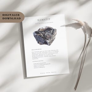 Può includere: Un download digitale con una pietra di ematite nera e grigia su una carta bianca. La carta include la parola "HÄMATIT" e testo in tedesco che descrive le proprietà della pietra, come radicamento e forza. Le parole "DIGITALER DOWNLOAD" sono nell'angolo in alto a sinistra.