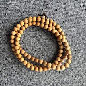 Puede incluir: Un collar de cuentas de madera marr&oacute;n claro, probablemente para meditaci&oacute;n o oraci&oacute;n. Las cuentas son redondas y est&aacute;n ensartadas, formando una forma circular. Una cuerda marr&oacute;n es visible en la parte superior, para colgar o usar.