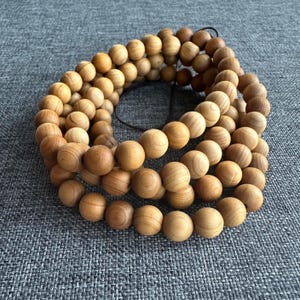 Puede incluir: Un conjunto de cuentas de madera marr&oacute;n claro, ensartadas en forma circular. Las cuentas son lisas y esf&eacute;ricas, con vetas de madera visibles. Probablemente para joyer&iacute;a o meditaci&oacute;n.