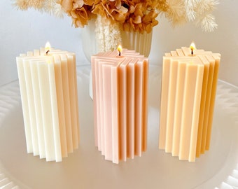 Pode incluir: Três velas de pilar com um design geométrico. As velas são em tons de branco, rosa claro e bege claro.