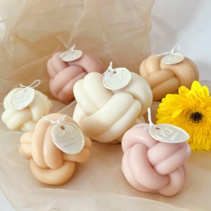 May include: Six knotted candles in various shades of pink, beige, and white. Each candle has a small, round label with the text "LMJ Candles" on it.