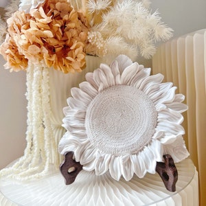 May include: White ceramic sunflower plate with a raised center and a textured surface. The plate is on a white stand with a brown base.