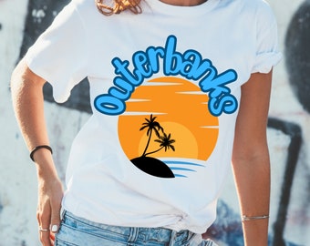 Może przedstawiać: Biała koszulka z niebiesko-pomarańczową grafiką przedstawiającą zachód słońca z palmami i tekstem "Outerbanks".
