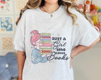 May include: A grey t-shirt featuring a graphic of a girl holding a stack of books. The text "Just a Girl Who Loves Books" is printed on the shirt.