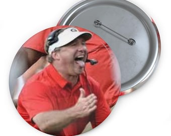 Könnte beinhalten: Ein runder Button mit einem Mann in einem roten Hemd und weißem Visier, mit offenem Mund und herausgestreckter Zunge. Der Button hat eine silberne Nadelrückseite und eine glänzende Oberfläche. Das Bild ist eine Nahaufnahme einer Person in einem roten Hemd.