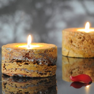 May include: Two round, yellow, textured candle holders with lit candles inside. The candle holders are made of natural stone and have a rustic look.