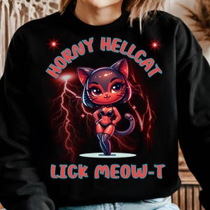 May include: Black sweatshirt with a cartoon graphic of a cat in lingerie, with the text "HORNY HELLCAT" and "LICK MEOW-T" in blue and red. The cat is red and black with lightning bolts in the background.