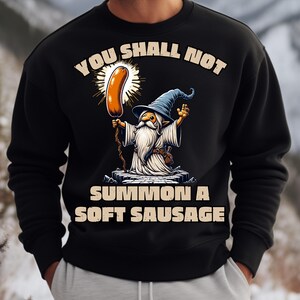 May include: Black sweatshirt featuring a wizard holding a sausage with the text "YOU SHALL NOT SUMMON A SOFT SAUSAGE". The wizard wears a blue hat and white robes. The sausage is brown and surrounded by a yellow glow.