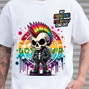 May include: White t-shirt featuring a cartoon skull with a rainbow mohawk, wearing a studded leather jacket and boots. The design includes a rainbow-colored background and the text "MY PRONOUNS ARE F*CK AROUND/ FIND OUT".