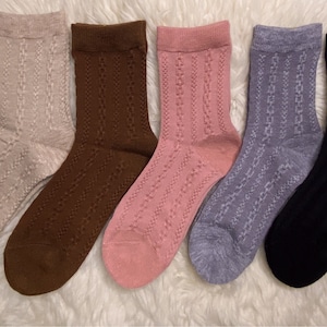 Könnte beinhalten: Fünf Paar gestrickte Socken in verschiedenen Farben: Beige, Braun, Rosa, Grau und Schwarz. Die Socken haben ein Zopfmuster.