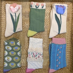 Könnte beinhalten: Sechs Paar bunte Socken mit verschiedenen Blumen- und geometrischen Mustern. Die Socken werden auf einer geflochtenen Korboberfläche präsentiert.