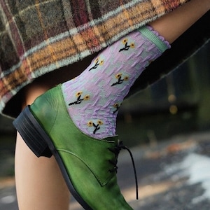 Könnte beinhalten: Ein Paar grüne Lederschuhe mit Schnürung und einer floralen Strumpfhose. Die Strumpfhose ist helllila mit gelben Blumen.