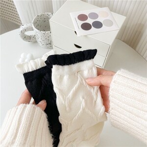 Könnte beinhalten: Zwei Paar Socken, ein Paar schwarz und ein Paar weiß. Beide Paare haben einen Rüschenrand und ein Zopfmuster.