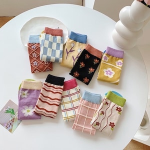 Könnte beinhalten: Sortiment an bunten Socken mit verschiedenen floralen und geometrischen Mustern. Die Socken liegen auf einer weißen Oberfläche.