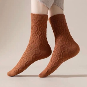 Könnte beinhalten: Ein Paar braune Socken mit einem strukturierten Rautenmuster. Die Socken sind kniehoch und aus weichem Material. Die Socken haben einen warmen, erdigen Farbton, ideal für Herbst- oder Winterkleidung.